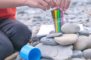 Close-up boy's hands puts markers while sitting on a stone beach on the shore of the sea.