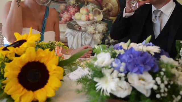 Fiori a centrotavola di un tavolo con due sposi che brindano e bevono due calici di spumante