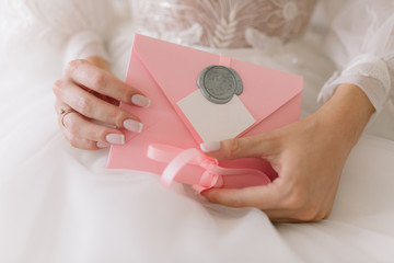 The bride holds an invitation to the wedding in a pink envelope.