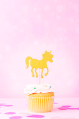 Creative pastel fantasy holiday card with cupcake, confetti and unicorn on bokeh backdrop. Baby shower, birthday, celebration concept.