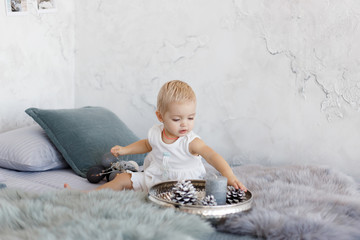 Fototapeta premium little baby girl in studio on bed. Beautiful little baby girl celebrates Christmas. New Year's holidays. Adorable baby girl playing with the garland on a gray background.