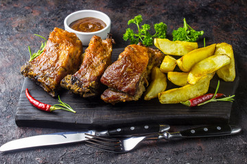 Barbecued pork ribs seasoned with a spicy bbq sauce served with fries on an old rustic wooden chopping board in a country kitchen