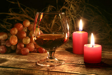 christmas candles, grapes and glass with cognac or whisky on wood background. Christmas decoration.