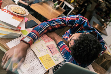 Late at night. Pleasant young man sleeping on the desk while studying a lot