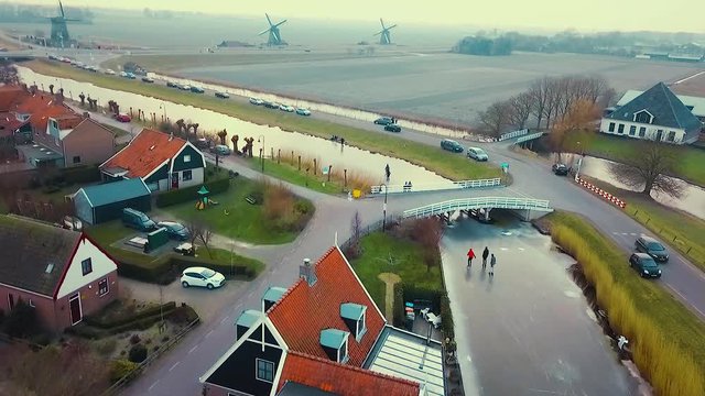 Drone shot of people ice skating underneath a bridge in Schermerhorn, a place in the Netherlands, with three traditional windmills in the background