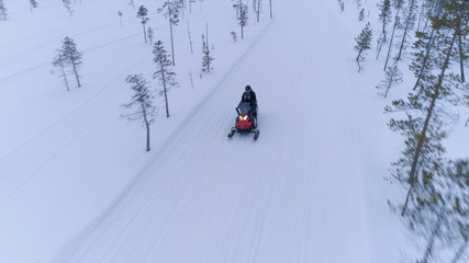 AERIAL, CLOSE UP: Couple riding snowmobile along snowy icy road in wintertime