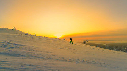 Fototapeta na wymiar AERIAL: Flying towards woman snowshoe trekking snowy mountain at winter sunrise