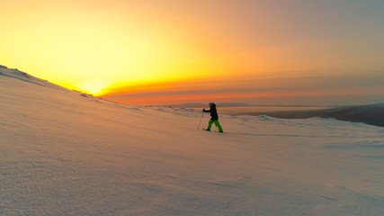 Fototapeta na wymiar AERIAL: Active woman exploring snowy Lapland wilderness on snowshoes at sunrise