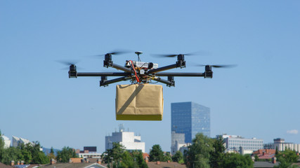 CLOSE UP: UAV drone delivery delivering big brown post package into urban city - obrazy, fototapety, plakaty
