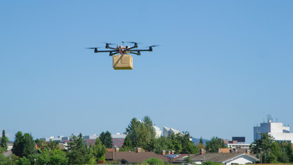 CLOSE UP: UAV drone logistics delivering big brown post package into urban city - obrazy, fototapety, plakaty