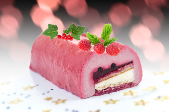 Yule log of raspberries fruits mousse, stuffed with raspberry puree sponge rolls, glazed with raspberry jelly, garnished with white chocolate, fresh berries, and gold leaf also know as Buche de Noel
