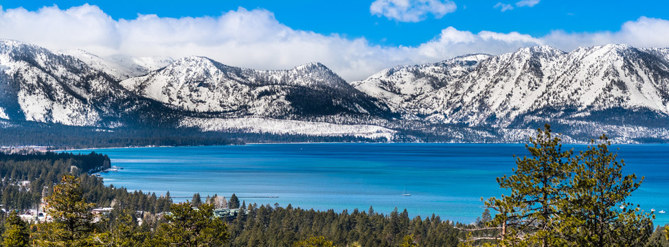 Panoramic view towards Lake Tahoe on a sunny clear day; the snow covered Sierra mountains in the background; evergreen forests in the foreground
