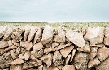 Typical stone wall of the island of menorca, with the meadow and the mediterranean sea in the background.