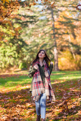 Fototapeta na wymiar A young brunette woman in a park surrounded by fall leaves.