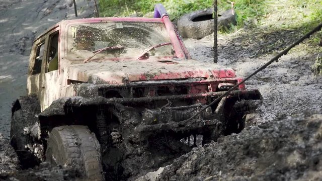 Close-up of the wheel of a car stuck in dirty water and dirt. The wheel turns, but it's helpless . electric winch pulls through the mud