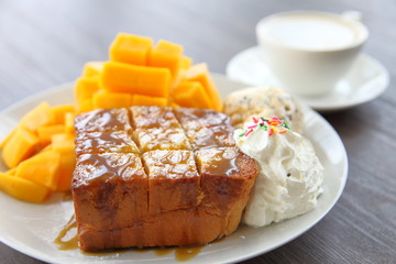Honey toast served as dessert with peeled decorative fresh mango with latte coffee on dark brown wooden table