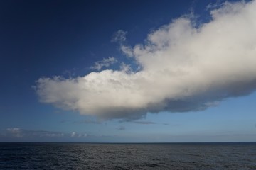 Thick white clouds over the horizon in a deep blue sky somewhere in the North Pacific Ocean between Sitka, Alaska, and Victoria, British Columbia, Canada.
