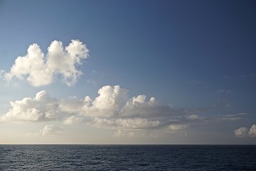 Thick white clouds over the horizon in a deep blue sky somewhere in the North Pacific Ocean between Sitka, Alaska, and Victoria, British Columbia, Canada.