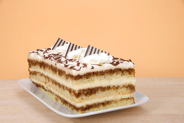 Tiramisu on a rectangular plate on wood table with orange background. Tiramisu is a popular Italian dessert with of layers of sponge cake soaked in coffee and brandy or liqueur.