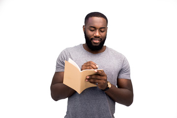 A young handsome African American man writes his plans for the week on a daily planner, is engaged...