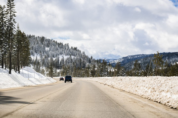 Cars driving on I80 interstate through the Sierra mountains close to lake Tahoe on a sunny winter day; the road has been cleared on snow, California