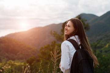 Back view of smiling girl with backpack in mountains