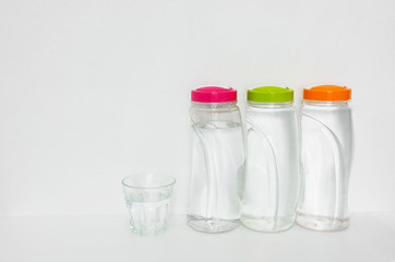 plastic bottles of drinking water and glass on white background, copy space