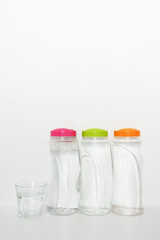 plastic bottles of drinking water and glass on white background, copy space