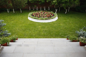 Stone steps down to the lawn with green grass and a round flower bed.