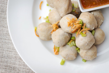 Boiled pork balls with sweet spicy sauce in white plate on gray table mat; top view