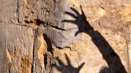 Strange shadow of two hands on an old stone wall. Black shadow, female hand. Background, texture, cropped shot, vertical, abstraction. Concept of fears.