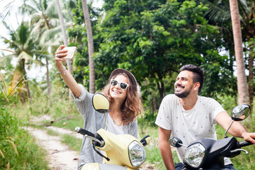 Attractive young couple on motorbikes in the jungle make selfie on smartphone, honeymoon in tropical countries, happiness, vacations, freedom