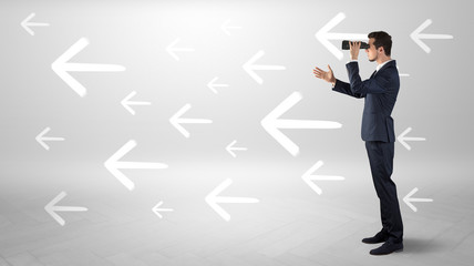 Young businessman standing and looking through binoculars with drawn arrows around
