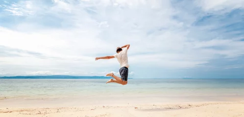 Fototapeten Young man in hat  jumping on the beach in front of ocean with feeling happy and freedom © olezzo