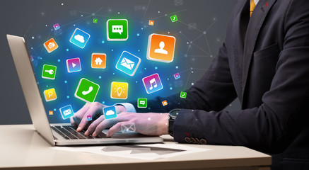 Businessman hand typing on laptop with flying application icons around
