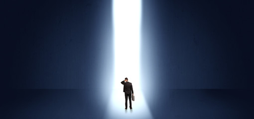 Businessman standing and seeing the light at the end of a big wall
