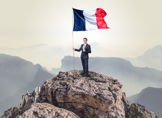 Obraz premium Successful businessman on the top of a mountain holding France victory flag 