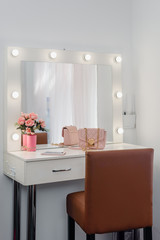 Square mirror with lamps and rose bouquet on visagist working place