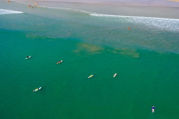 Aerial drone view of surfers waiting for waves in a shallow, tropical ocean