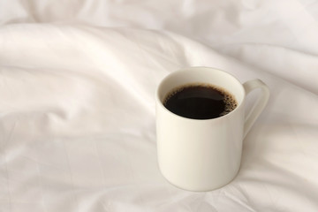 Black coffee cup on the unmade bed in cozy morning with sunshine into window.