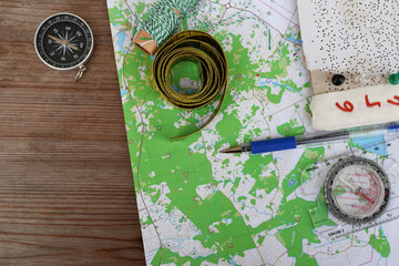 Top view of topographic map for orienteering or rogaining sport, compass and other accessories on brown wooden background with copy space for text.