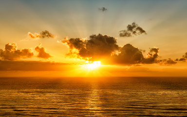 scenic sunset over pacific ocean with setting sun rays coming through dramatic clouds on orange...