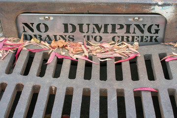 No Dumping drains to creek - warning sign on steel plate guards drain inlet near grating storm...