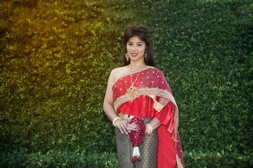 The pretty Thai lady in Middle Thai classical traditional dress suit standing and hold garland is posing in a park.