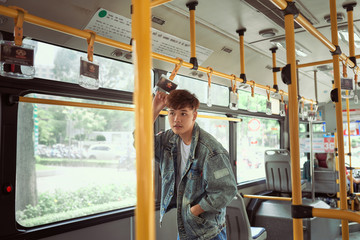 Young cheerful handsome man is holding onto the bar while standing in a bus.