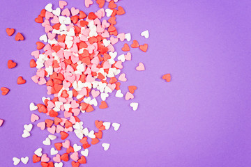 Many small multicolored sweet hearts are scattered on a violet background. Border. Flat lay. Copy space.
