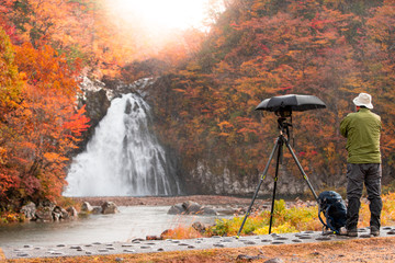 Male photographer Raining to photograph waterfall in leaves change color. In Akita, Japan