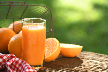 Fresh orange juice in glass with sliced orange on wood and nature background