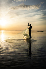 Fototapeta premium Silhouette of traditional fishermen throwing net fishing at sunrise time, livelihoods of fishermen at Pakpra, Phatthalung in Thailand