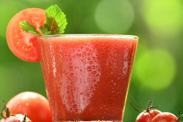 Blended tomato juice with slice tomatoes in glass on nature background